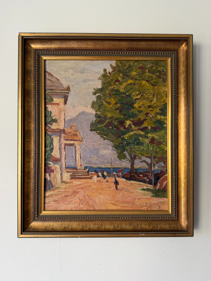 A framed vintage oil painting depicting a coastal scene with a classical building, a large green tree, a sandy path, and distant mountains, housed in an ornate gold frame. Available at Hue. 