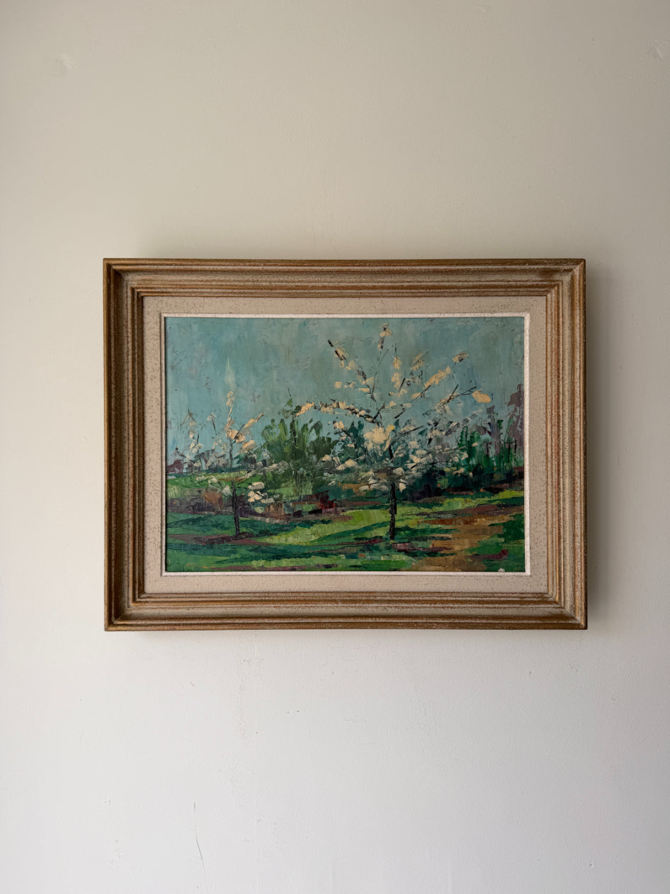A framed vintage landscape oil painting featuring blossoming trees in a green field under a blue sky, housed in a rustic brown wooden frame. Available at Hue.