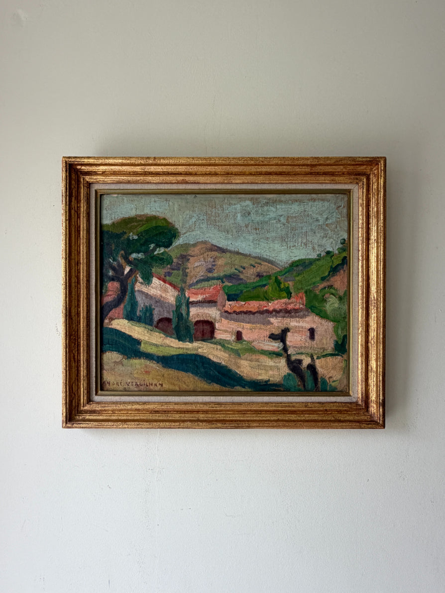 A framed vintage oil painting of a Mediterranean village landscape, featuring a rustic stone building with red-tiled roofs, green hills, and a blue sky, housed in a distressed gold frame. Available at Hue. 