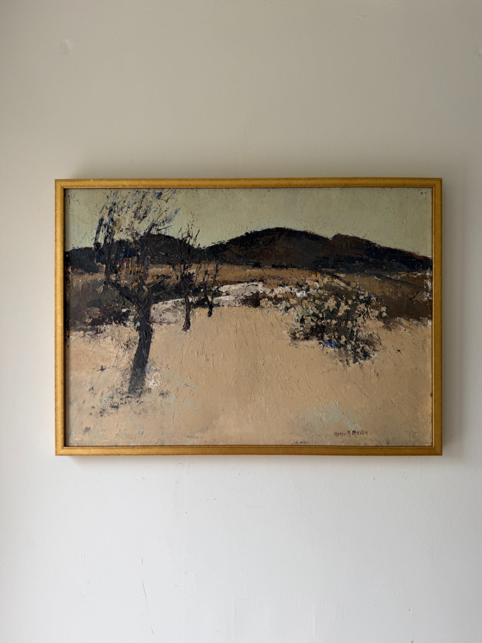 A framed vintage landscape painting. The artwork depicts a dry, sandy scene with a dark tree in the foreground, sparse shrubs, and dark hills under a pale sky. Available at Hue. 