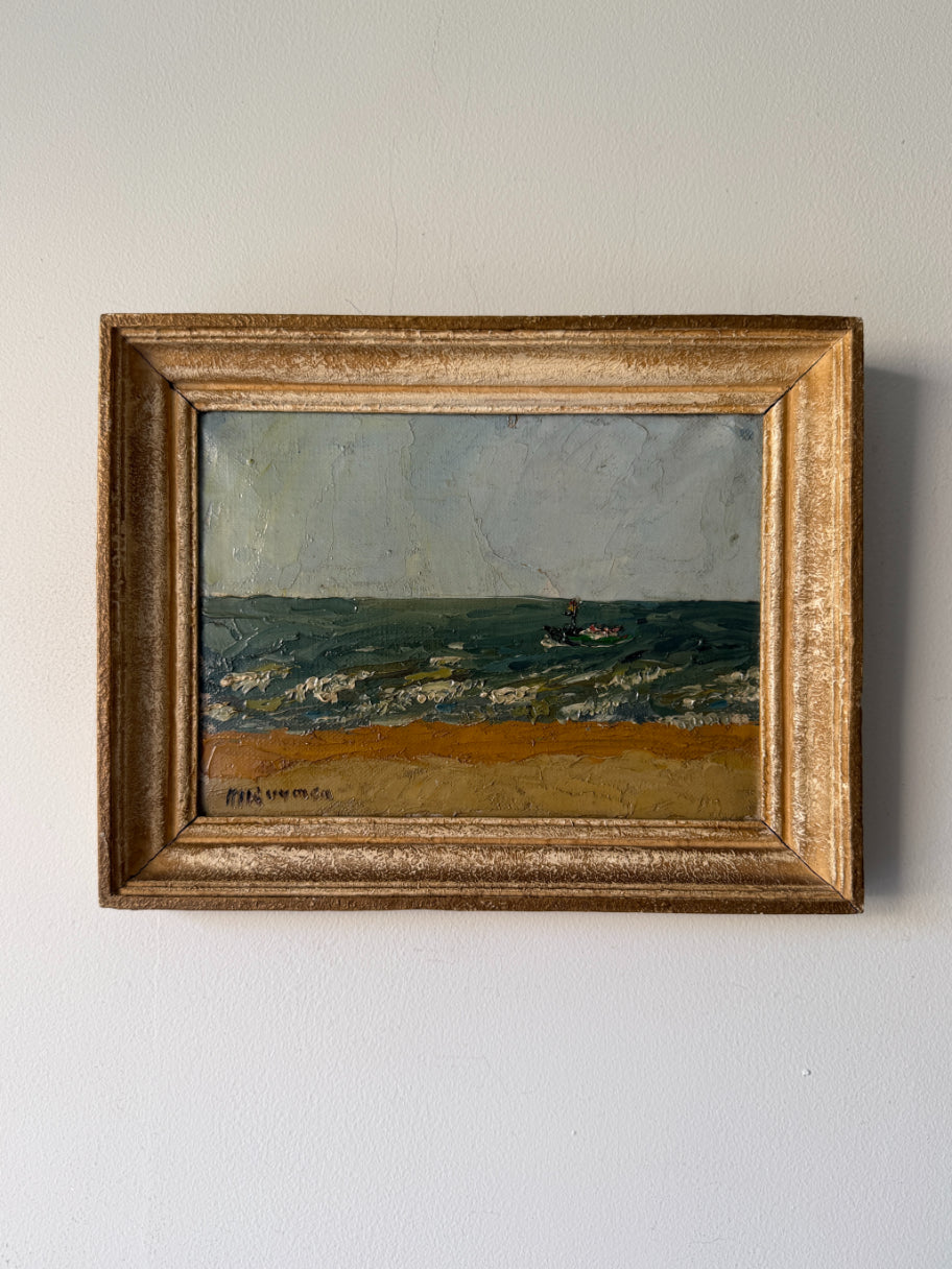A framed vintage oil painting of a coastal landscape with a sandy beach, blue-green sea, and a small boat under a pale sky, housed in an ornate gold frame. Available at Hue. 