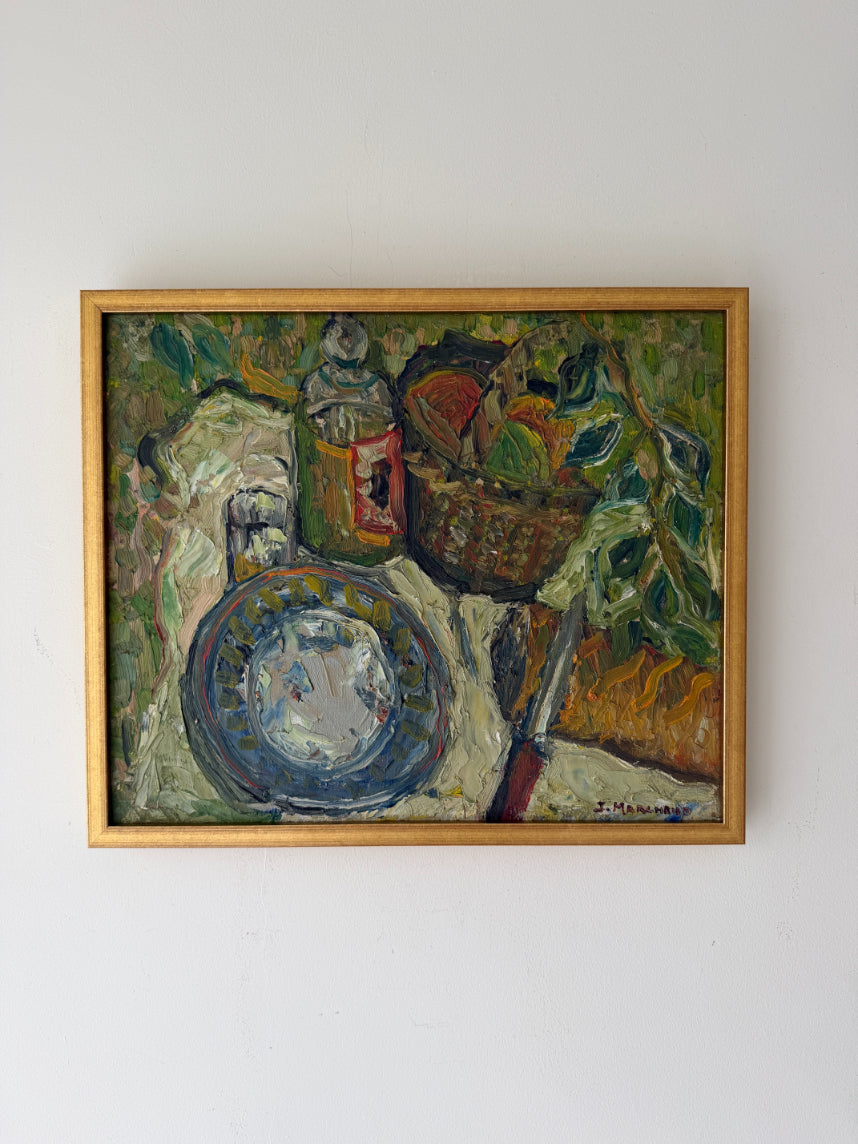 A framed vintage still life oil painting depicting a blue patterned plate, a basket of fruit, and bottles on a draped tablecloth. Available at Hue. 