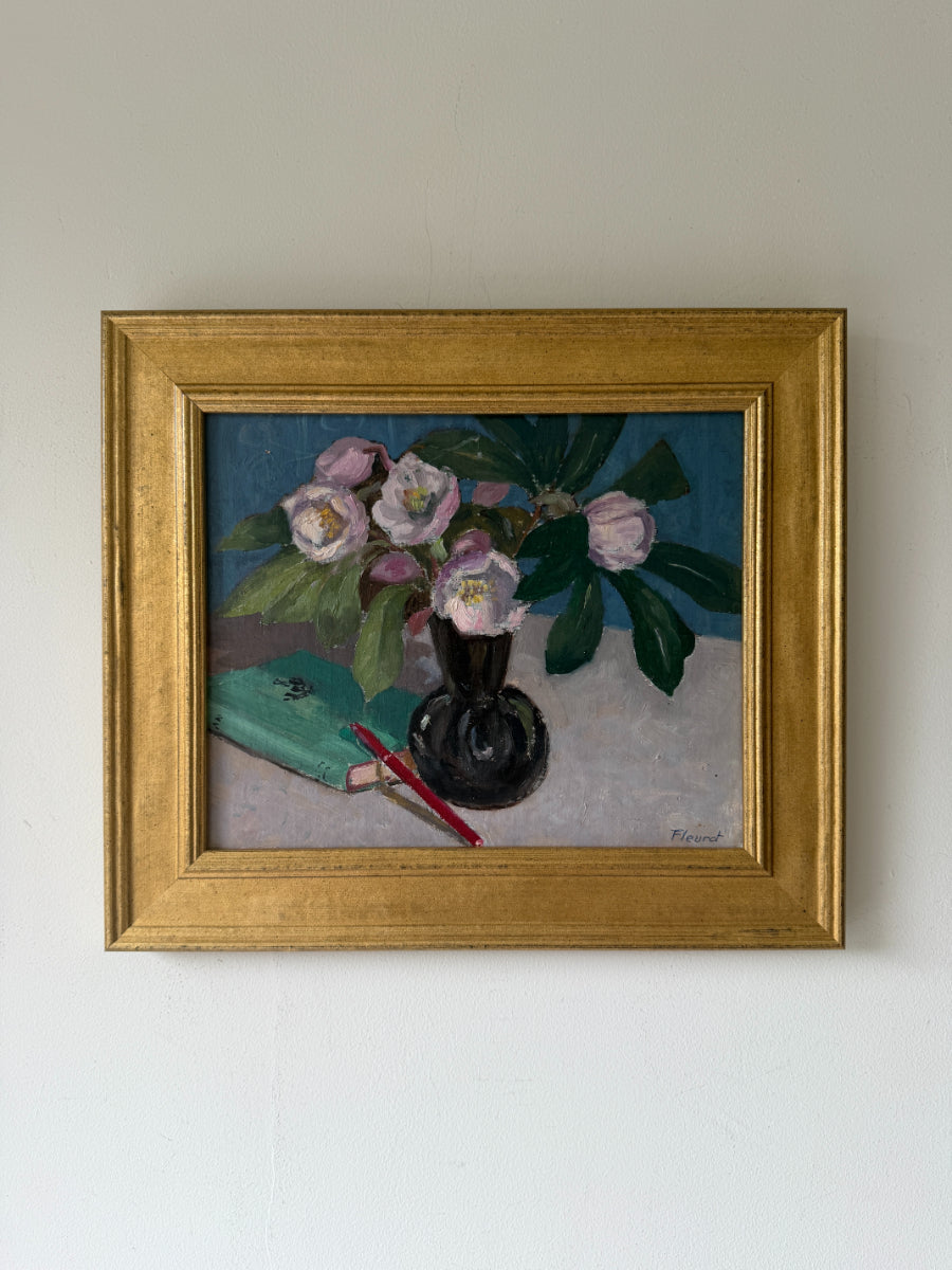 A framed vintage still life oil painting featuring pink flowers in a dark vase with green leaves, alongside a teal notebook and red pen. Available at Hue. 