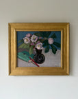 A framed vintage still life oil painting featuring pink flowers in a dark vase with green leaves, alongside a teal notebook and red pen. Available at Hue. 