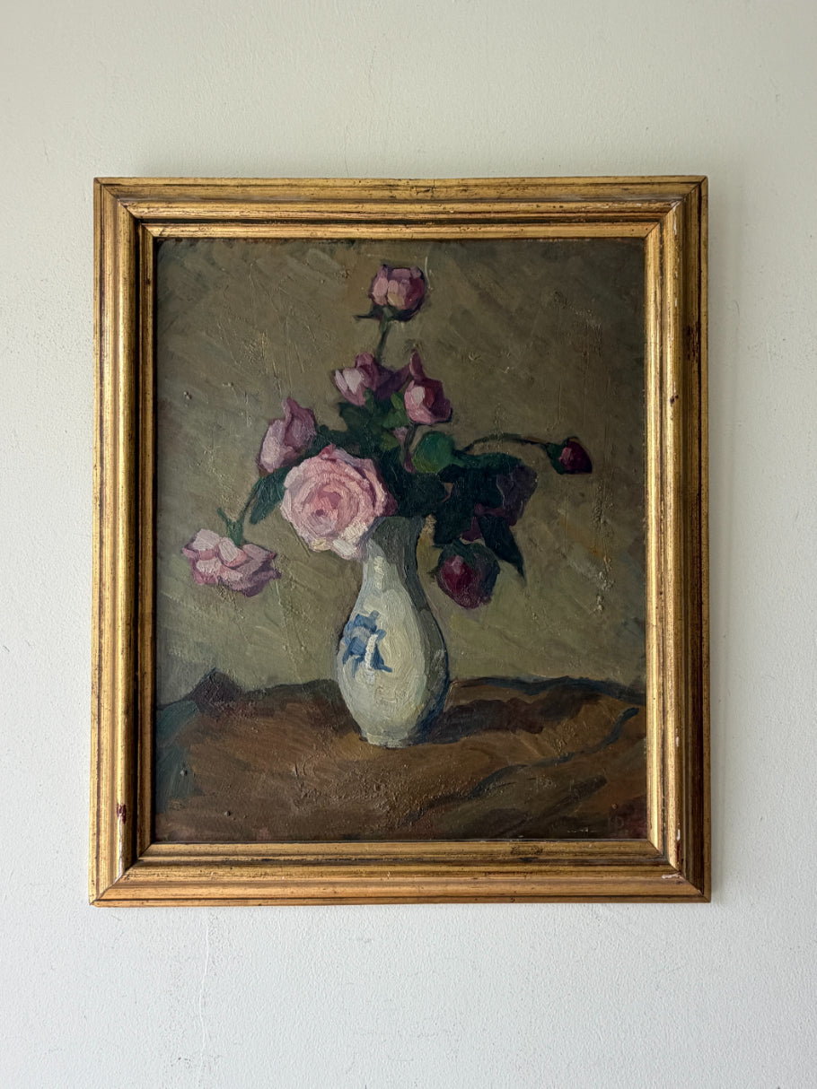 A framed vintage oil painting of pink roses in a white vase. The painting features a textured olive background, with the flowers in shades of pink and purple, and is enclosed in a distressed gold frame. Available at Hue. 