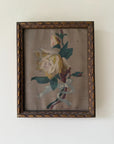 A framed vintage oil painting depicting a pale yellow rose with green leaves and a white ribbon, set in an ornate dark brown wooden frame. Available at Hue. 