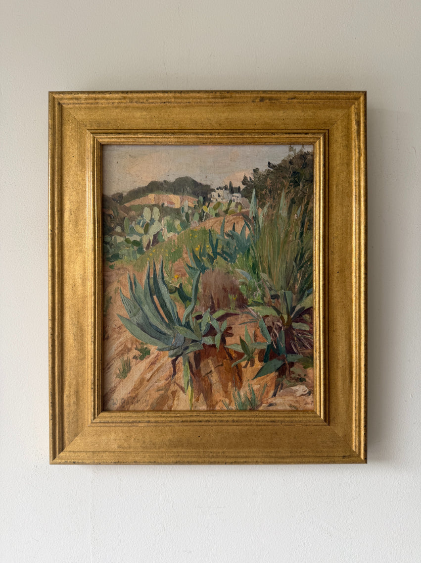 A framed vintage landscape oil painting featuring green succulents and cacti in a dry, rocky terrain, housed in a wide, ornate gold frame. Available at Hue.