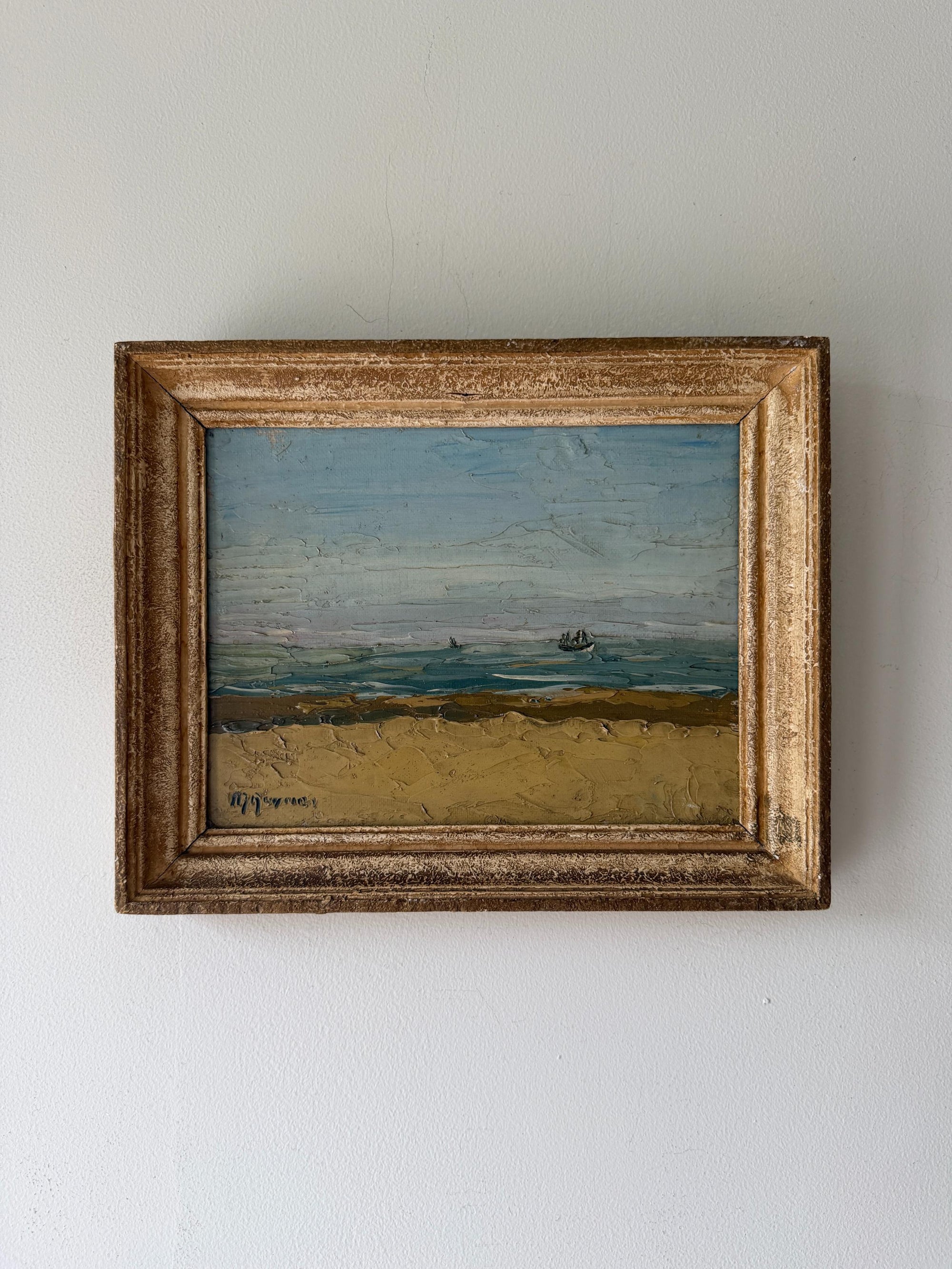 A framed vintage landscape oil painting depicting a sandy beach and blue sea under a cloudy sky. Available at Hue. 