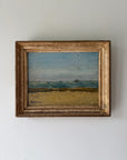 A framed vintage landscape oil painting depicting a sandy beach and blue sea under a cloudy sky. Available at Hue. 