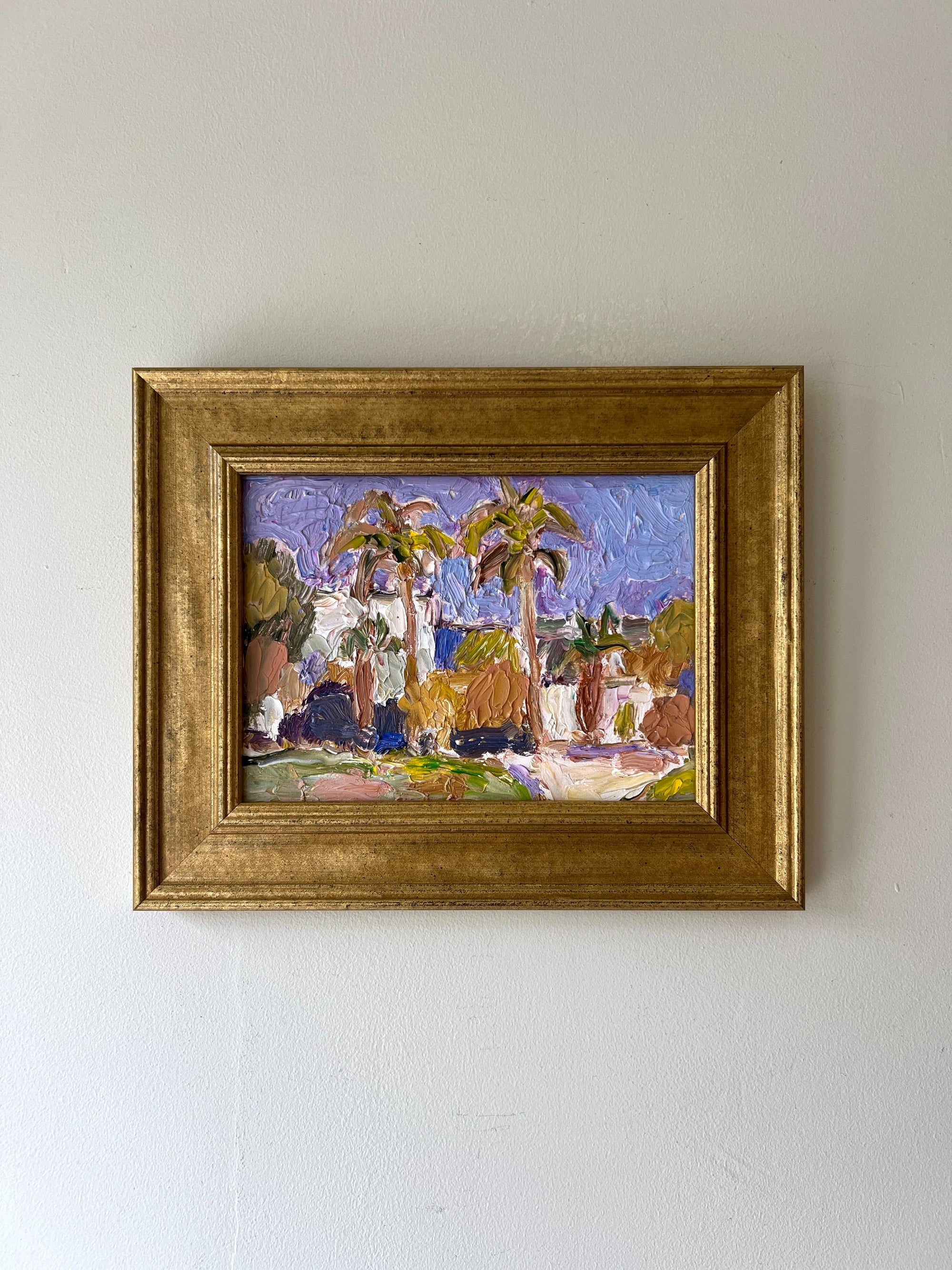 A framed vintage landscape oil painting of palm trees and a small coastal village. Available at Hue. 
