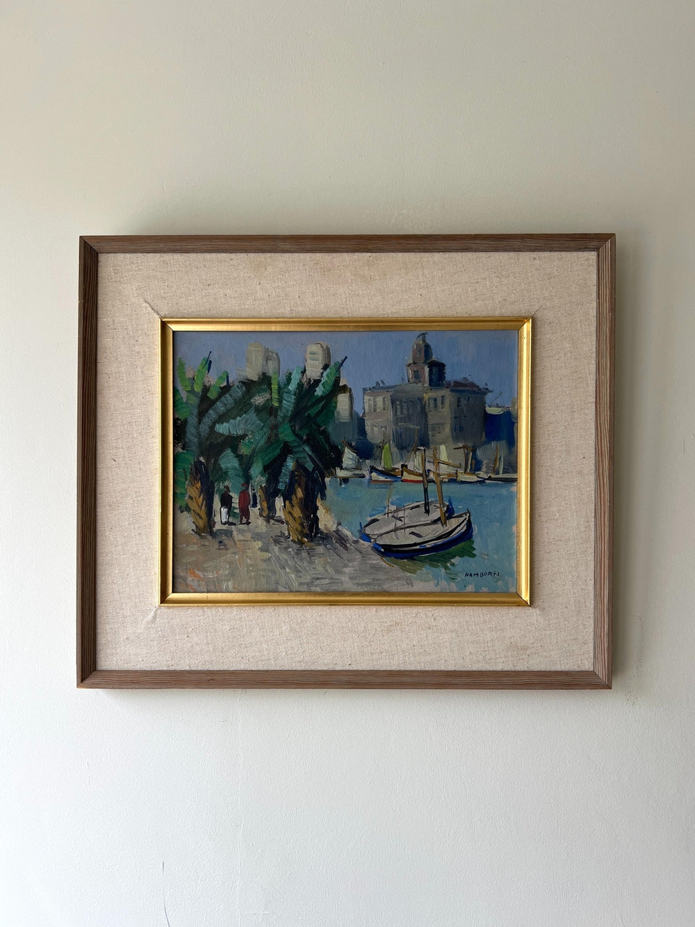 Framed painting of a coastal scene with buildings and boats on a white wall available from hue