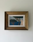 A framed oil painting featuring a minimalist landscape with blue water and dark green trees. Available at Hue. 
