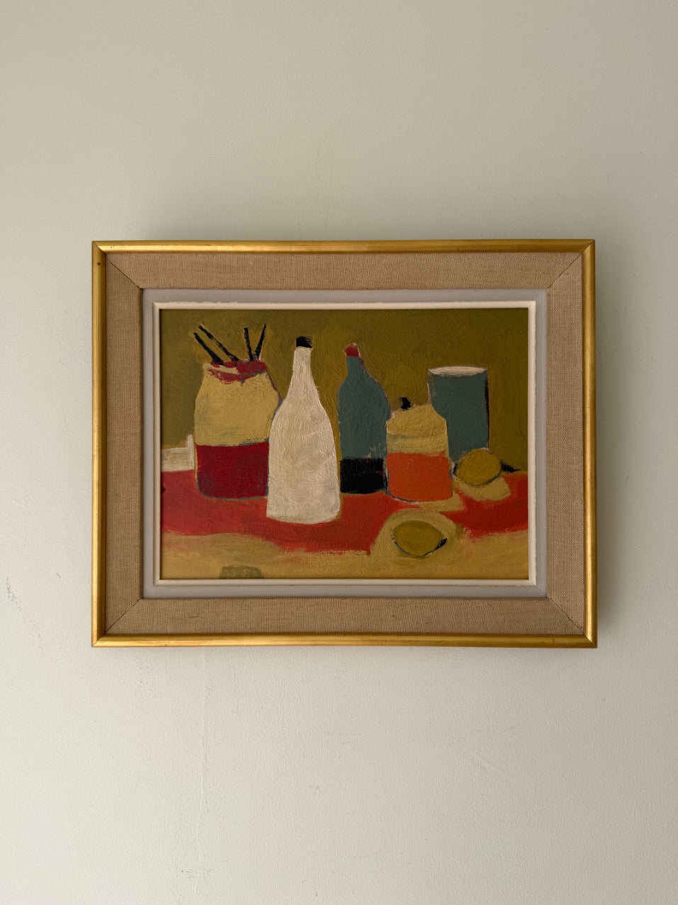 A framed still life oil painting featuring stylized bottles and objects on a table, with a gold frame. Available at Hue.