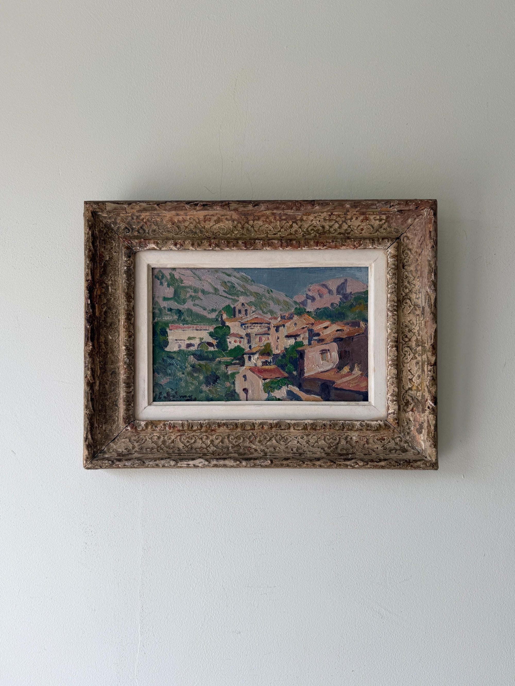 A framed vintage landscape oil painting of a hillside village with green trees and terracotta roofs. Available at Hue. 