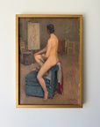 A framed vintage oil painting depicting a nude woman seated on a blue armchair in an artist studio, with a canvas and easel in the background. Available at Hue. 