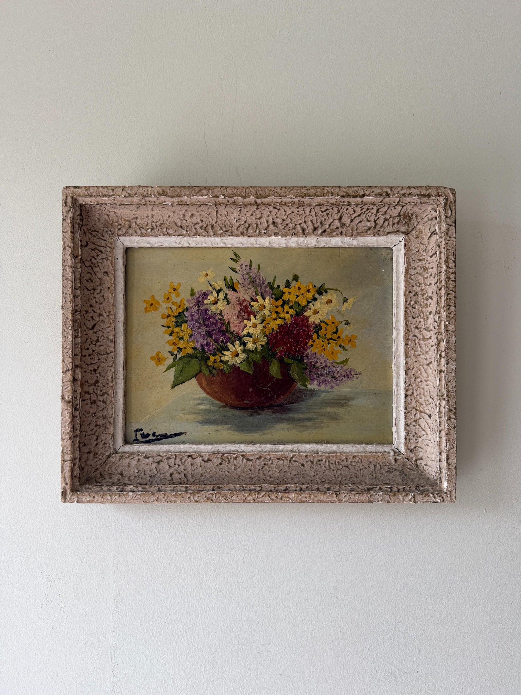 A vintage framed still life painting of a colorful flower bouquet in a dark red bowl, set against a neutral beige background. Available at Hue. 
