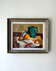 Framed vintage still life oil painting with a teal green pitcher and fruits on a striped cloth. Available at Hue. 