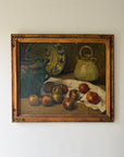 A framed vintage still life oil painting depicting apples, a green jug, a patterned plate, and a ceramic pot on a draped cloth. Available at Hue. 