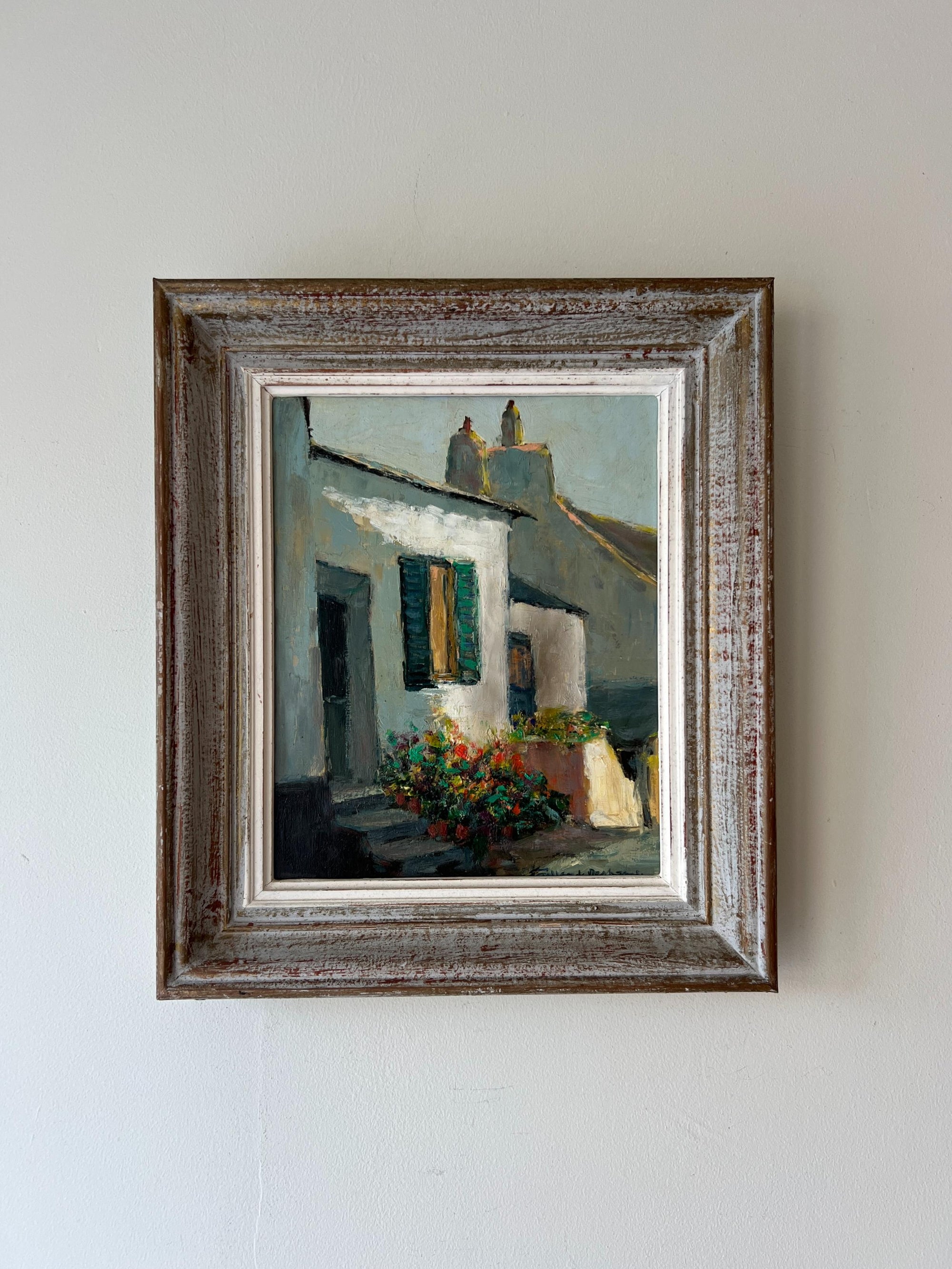 Framed vintage oil painting of a village scene with red flowers by the doorways. Available at Hue. 