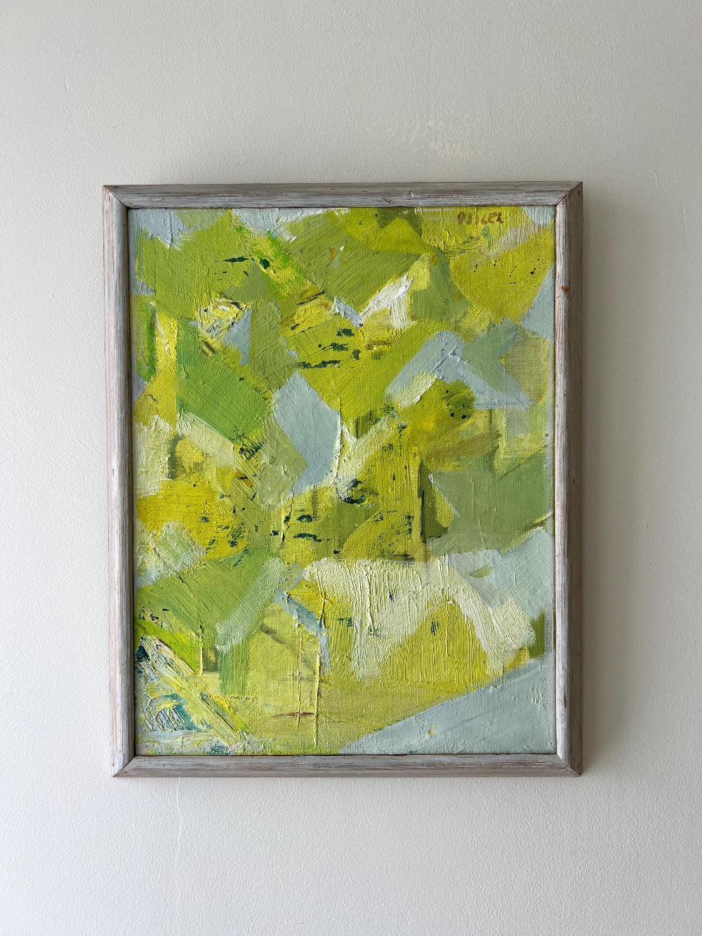 Abstract painting with green and blue tones in a silver frame on a white wall available from hue