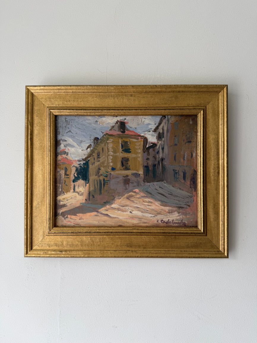 A framed vintage impressionist oil painting of a European street scene with yellow and ochre buildings. Available at Hue.