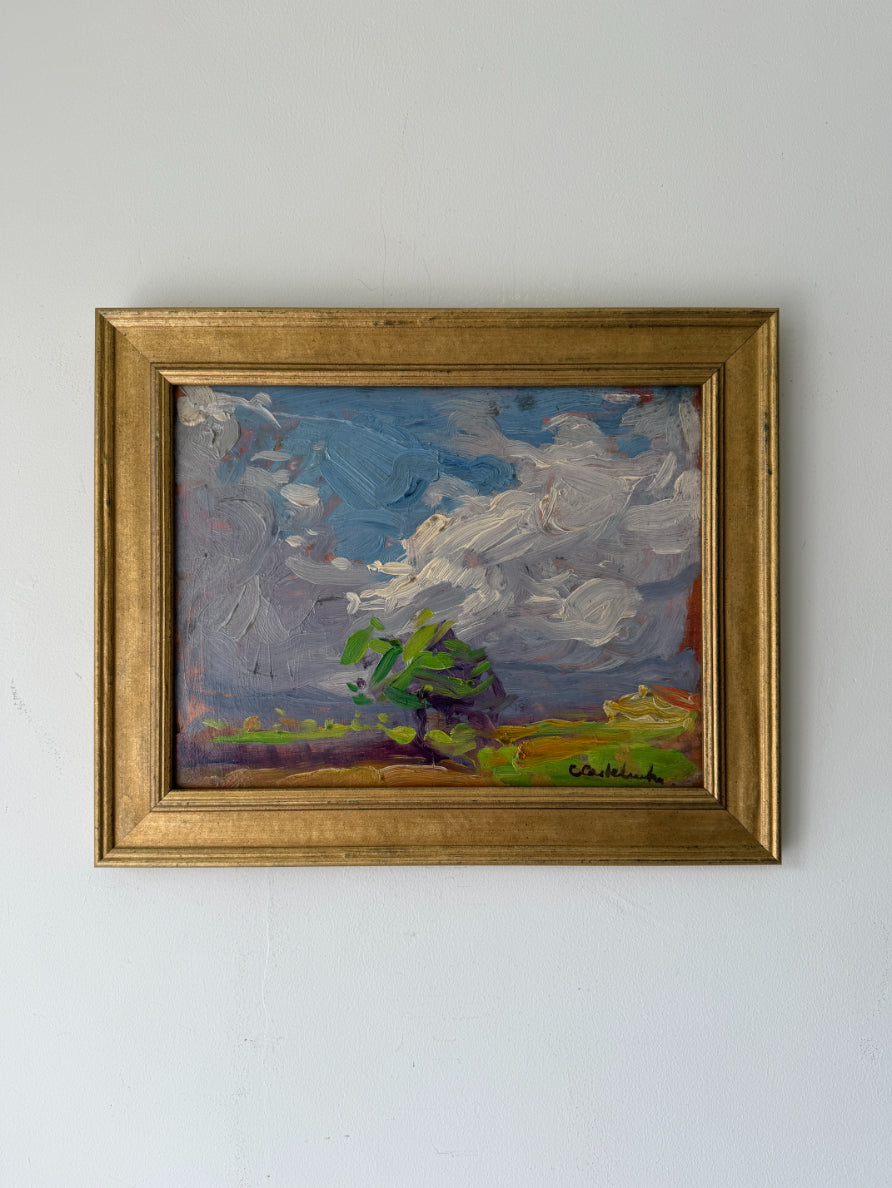A framed vintage landscape oil painting featuring a green tree under a dramatic blue and white sky. Available at Hue. 