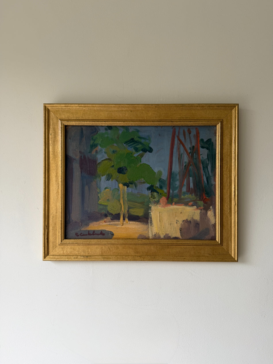 A framed vintage oil painting depicting a garden scene with green trees and a table. Available at Hue.