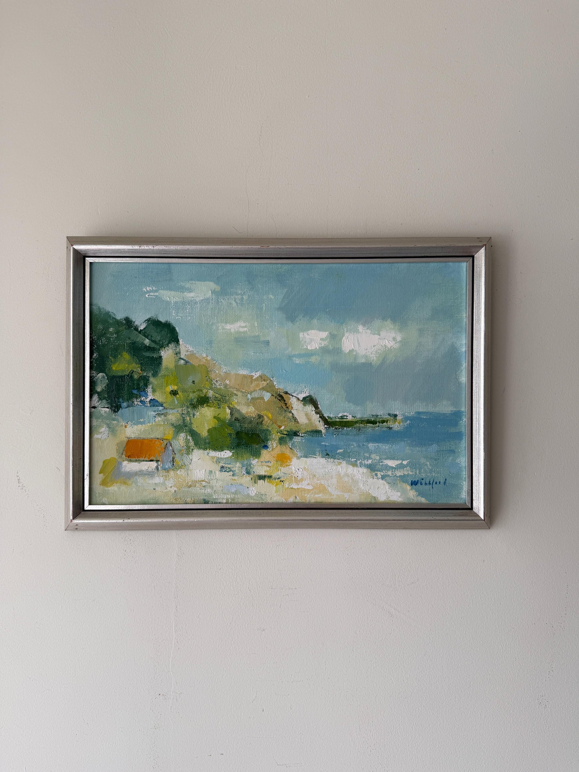 A framed vinatge landscape oil painting depicting a coastal scene with blue water, green trees, and a sandy shore. Available at Hue. 