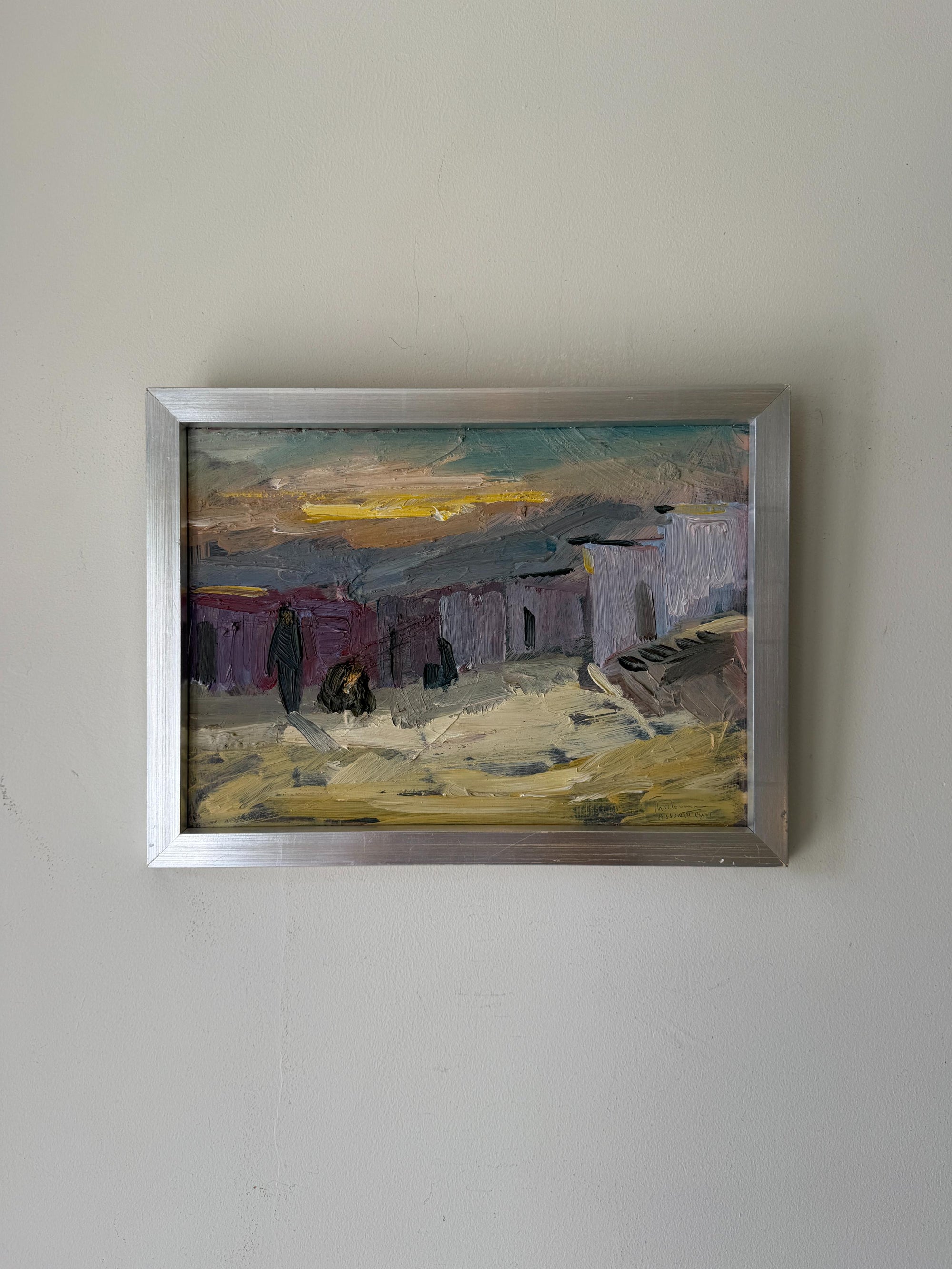 A framed vintage landscape oil painting with an impressionistic style, featuring muted buildings, yellow and green sky, and a silver frame. Available at Hue.