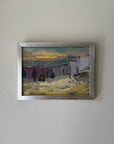 A framed vintage landscape oil painting with an impressionistic style, featuring muted buildings, yellow and green sky, and a silver frame. Available at Hue.