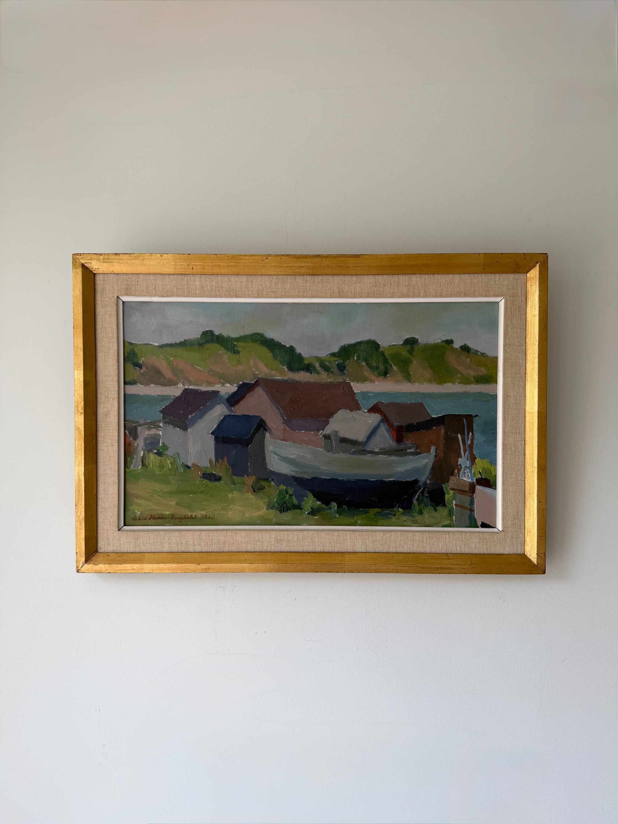 A framed vintage landscape painting of a coastal village with a boat. Available at Hue.
