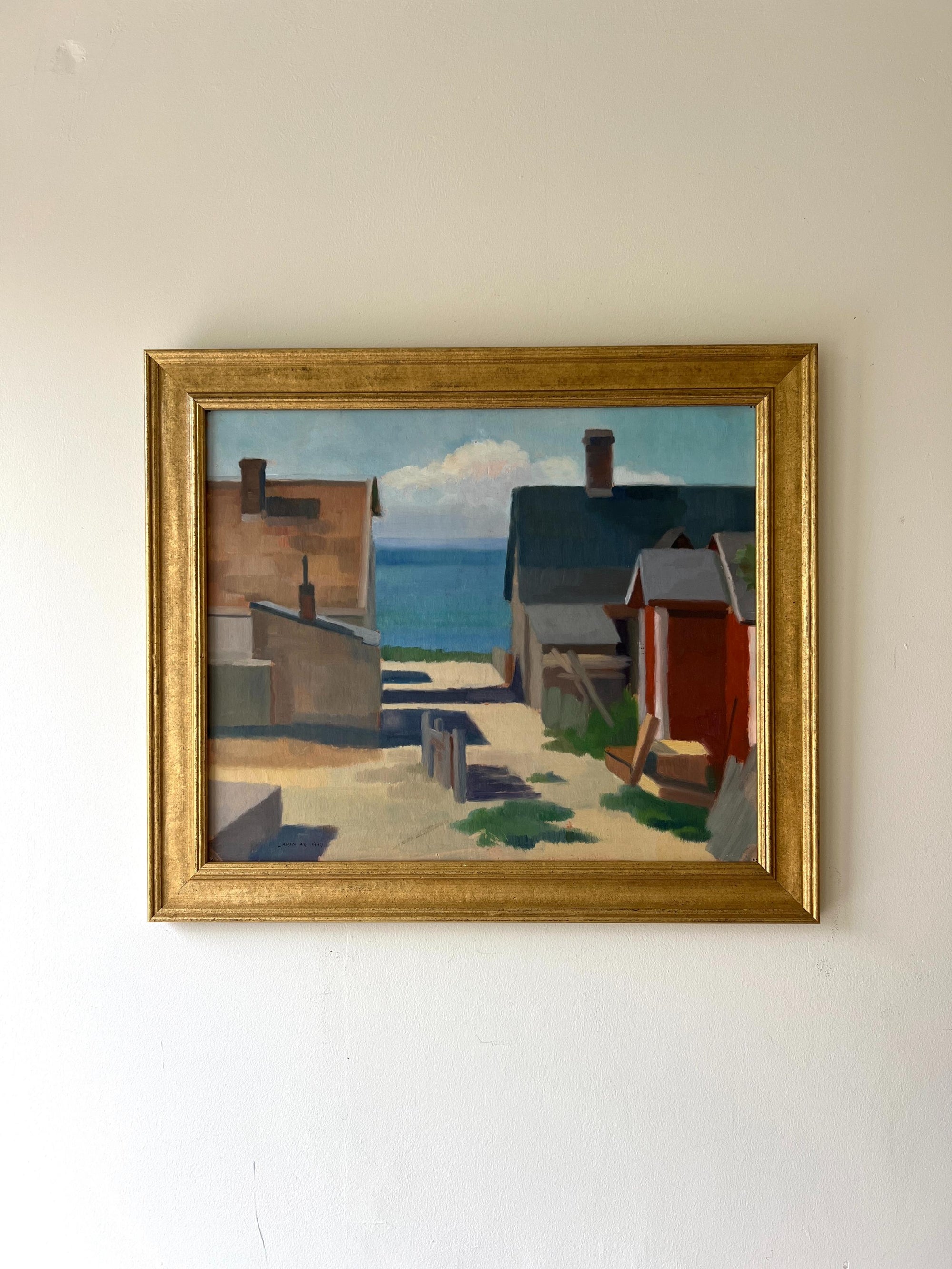 A framed vintage oil painting of a village harbour. Available at Hue. 
