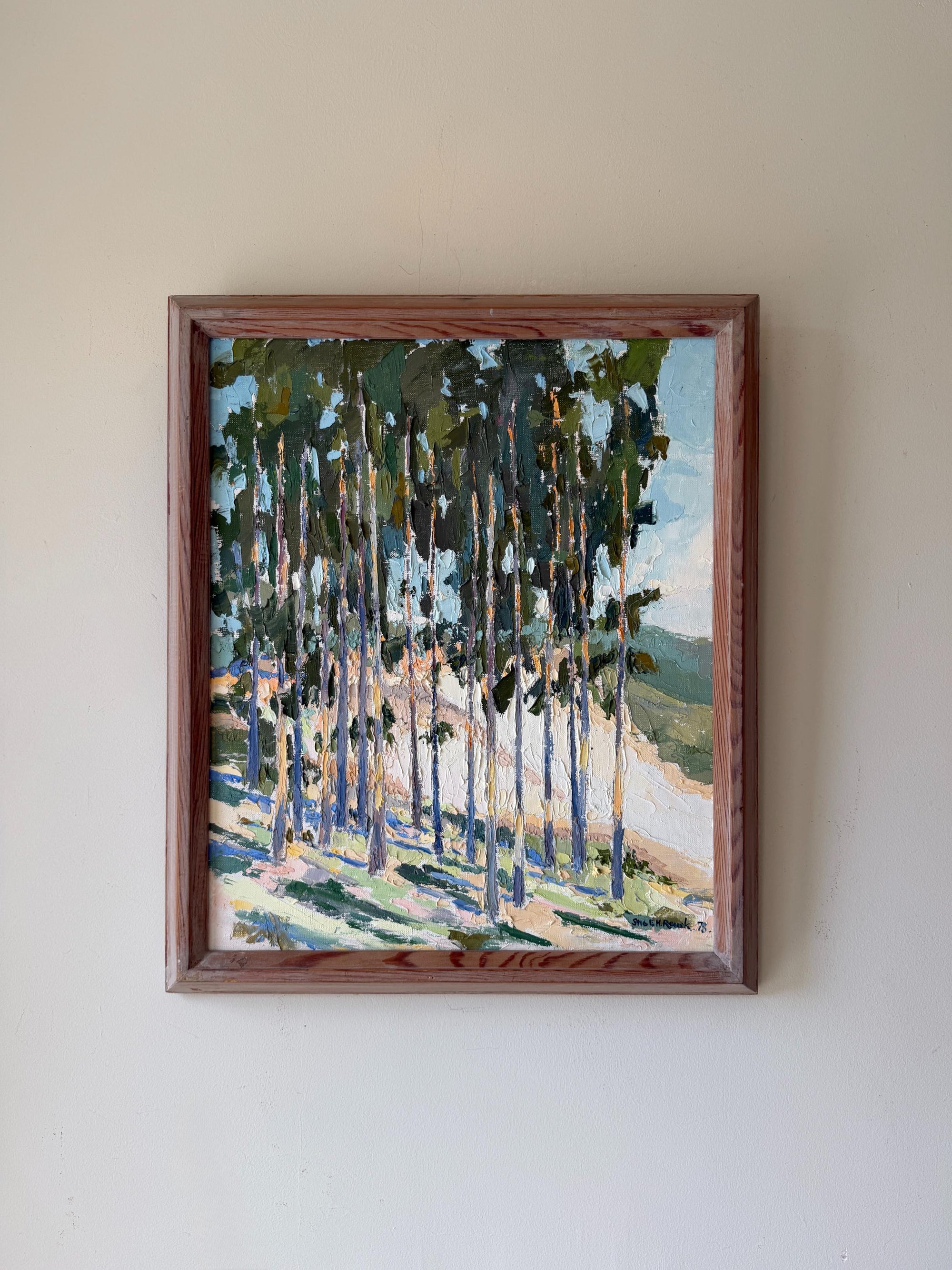 A framed vinatge landscape painting of a forest with tall trees, painted in green, blue, and beige tones. Available at Hue. 
