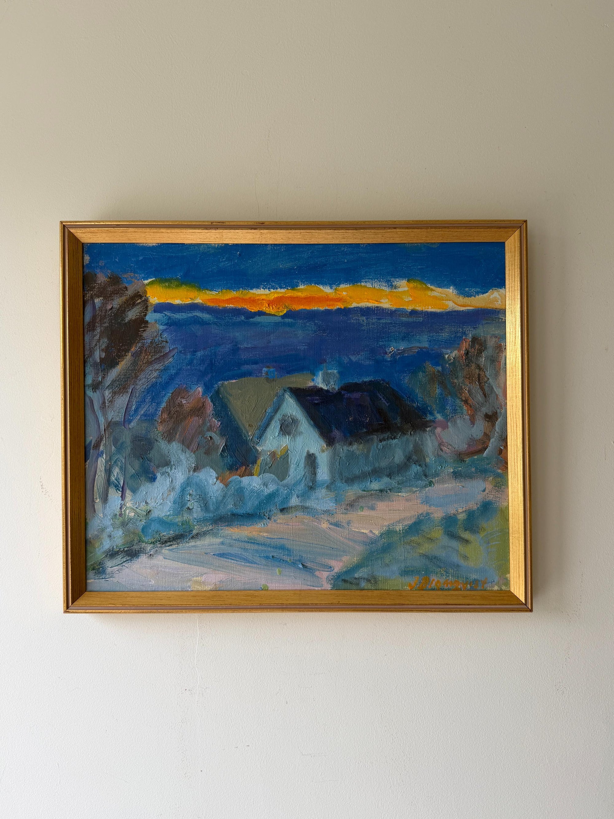 A framed vintage landscape oil painting of a house in a village under a blue sky with a yellow sunset. Available at Hue. 