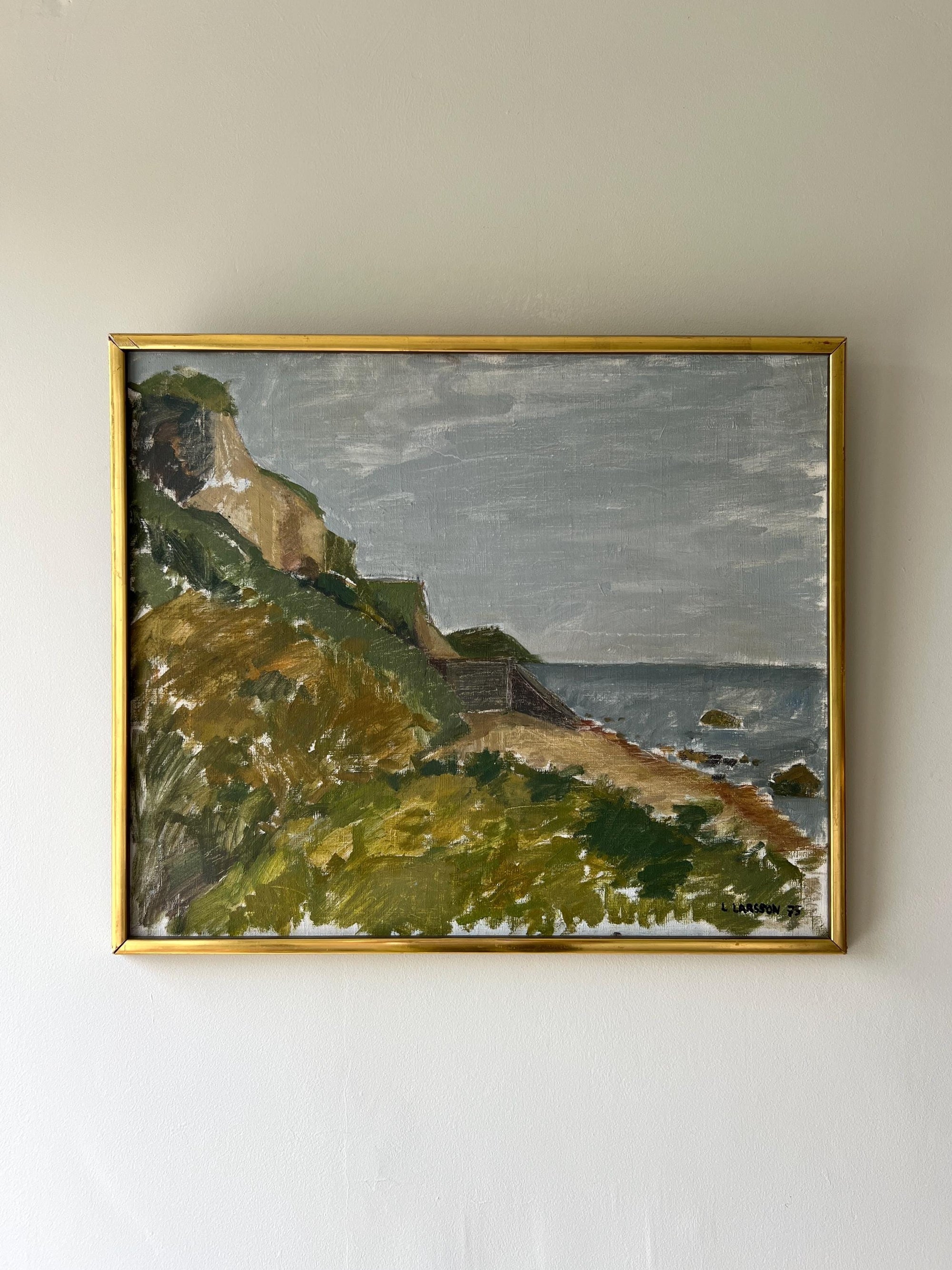 Framed vintage oil painting of a coastal landscape with greenery and water in a slim gilt frame, available at Hue.