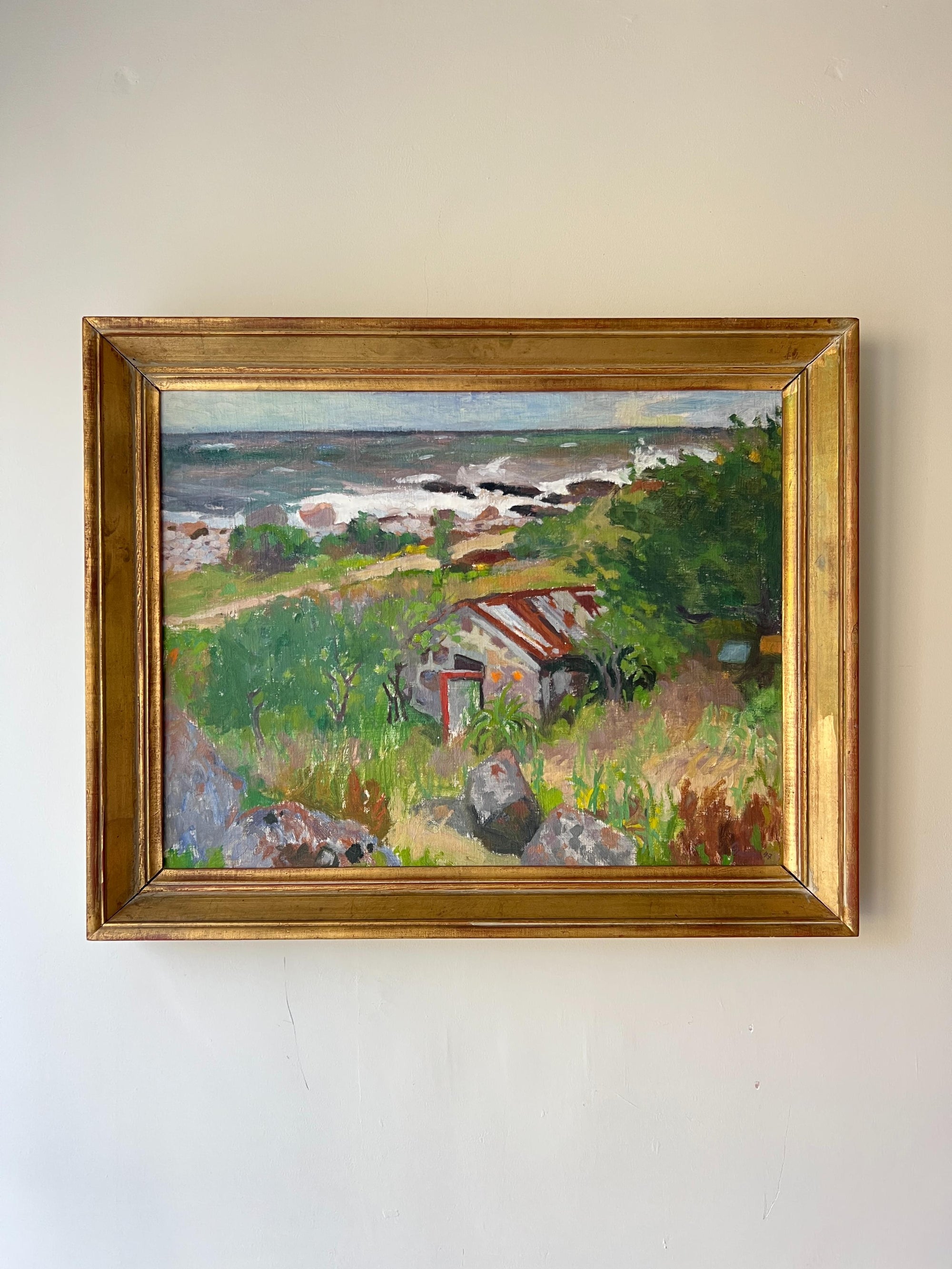 Framed vintage oil  painting of a coastal landscape with wild greenery and a cottage. Available at Hue. 