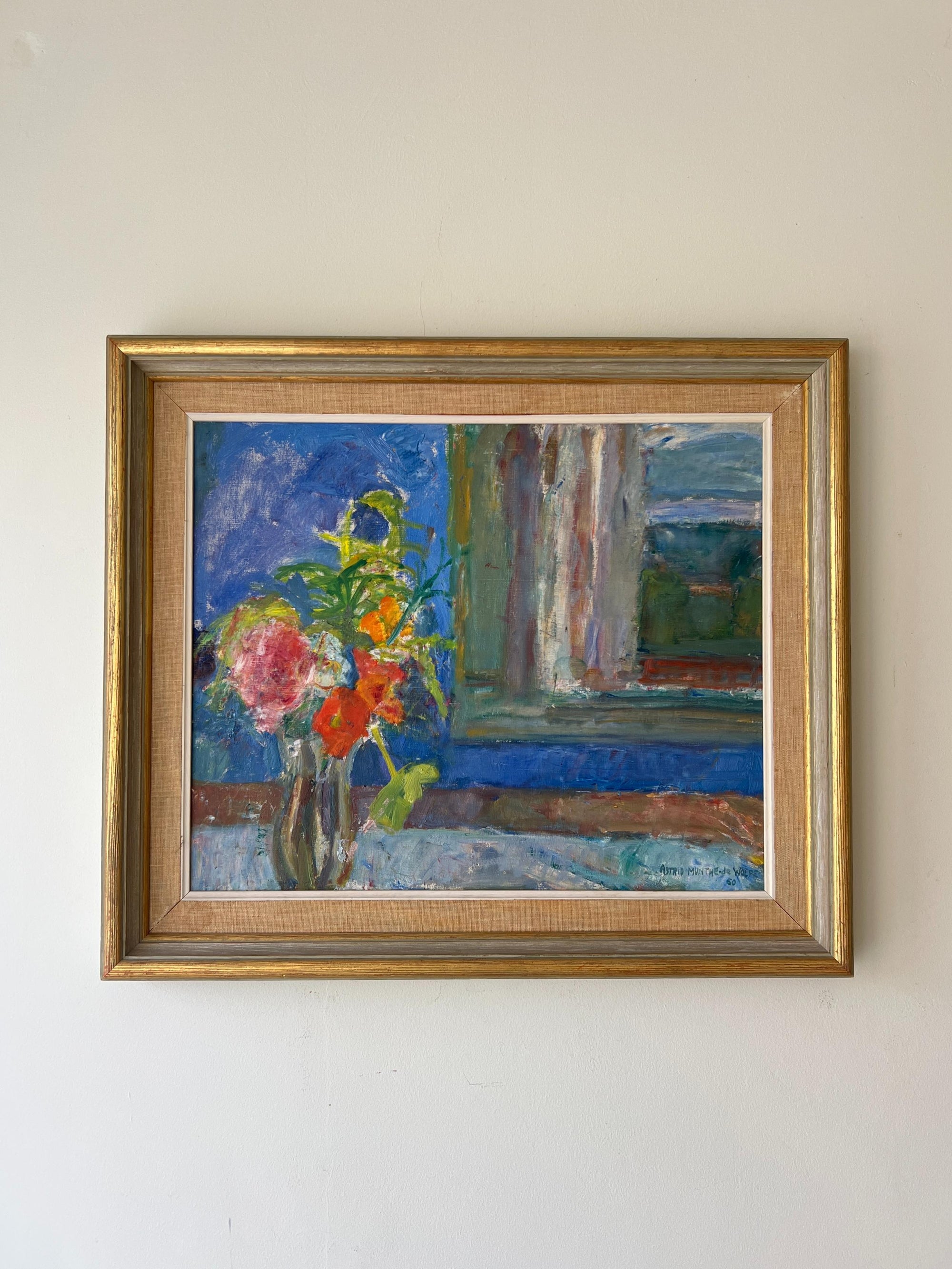 A framed vintage oil painting of a bouquet in front of a blue wall and window. Available at Hue.