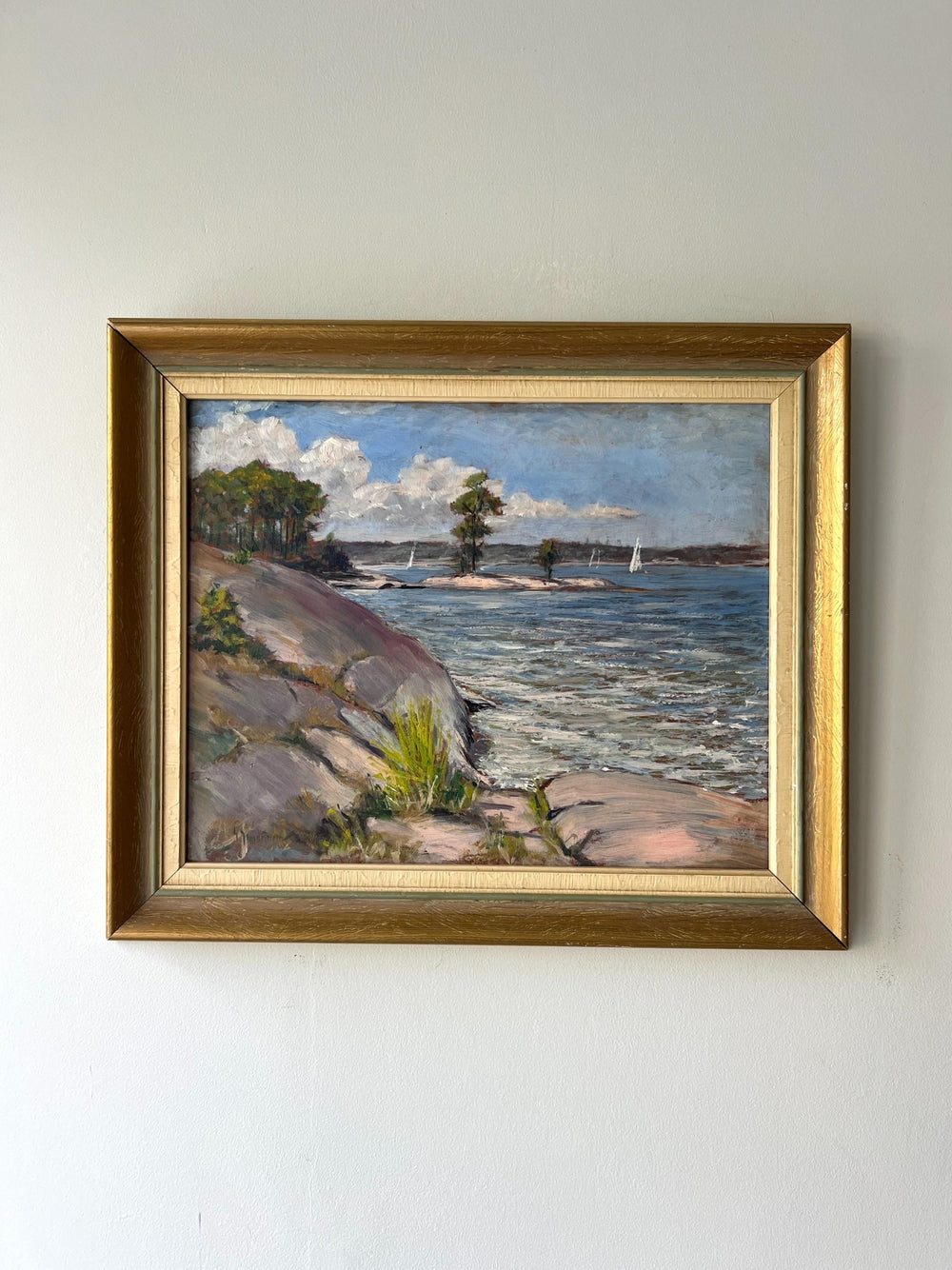 Framed painting of a coastal scene with rocky shore and water on a white wall available from hue
