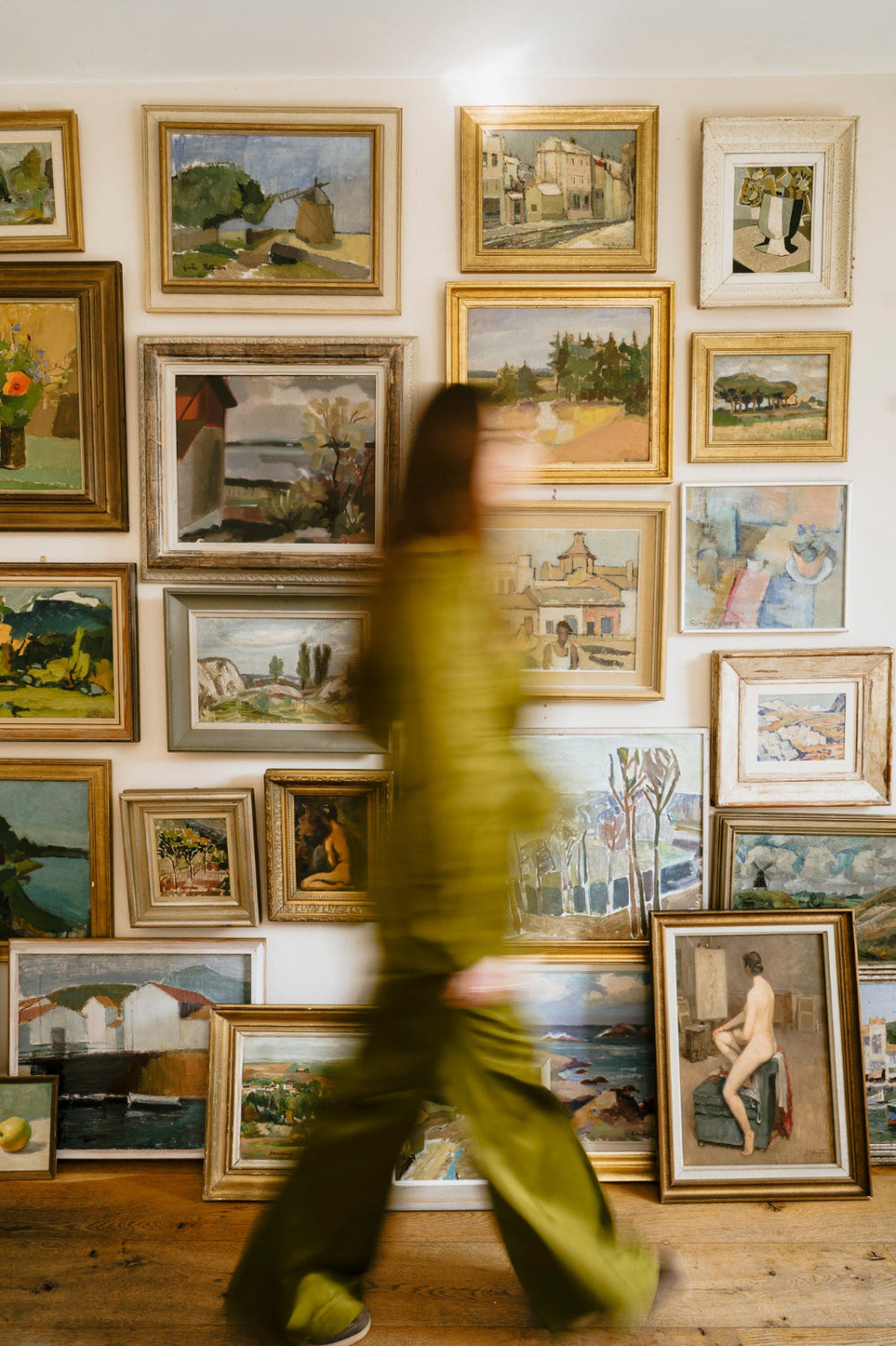 Gallery wall of original vintage art and vintage oil paintings with a person walking past the collection.