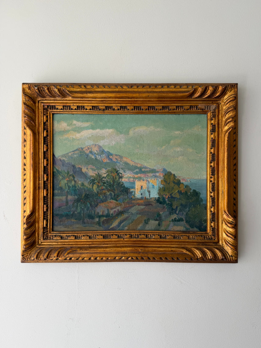 A framed vintage landscape oil painting featuring a mountain, palm trees and coastline, housed in an ornate gold frame. Available at Hue. 