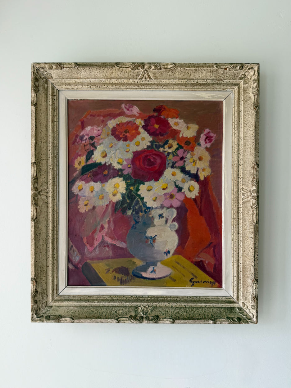 A framed vintage still life painting of a flower bouquet in a vasel. The artwork features a mix of red, white, yellow, and pink flowers with a blue-gray vase, enclosed in an ornate distressed silver frame. Available at Hue. 