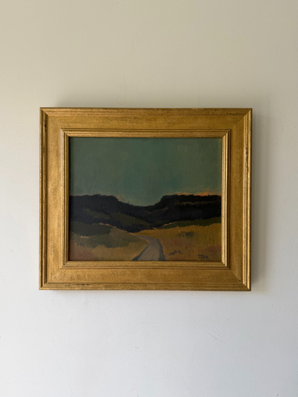 A framed vintage landscape oil painting depicting a winding road leading through dark hills under a muted green sky, enclosed in a gold frame. Available at Hue.