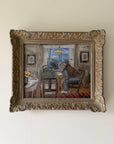 A framed vintage oil painting of two figures sitting at a table in a room, housed in an ornate, carved gold-toned frame. Available at Hue. 