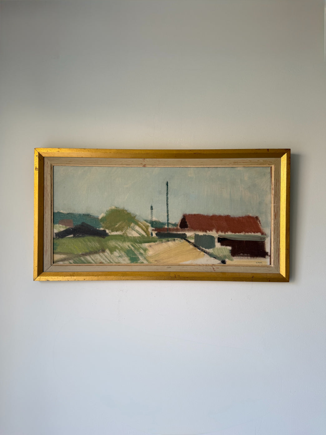 A framed vintage landscape  oil painting depicting a rural scene with a red-roofed house, green fields, and a pale sky. Available at Hue. 