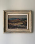 A framed vintage landscape oil painting. The scene depicts a field with distant hills and small red houses. Available at Hue.