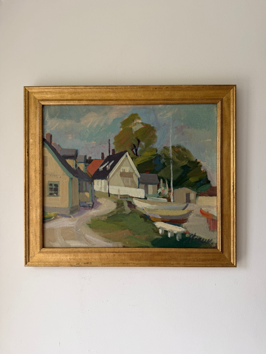 A framed vintage landscape oil painting depicting a coastal village with houses, boats, and trees, housed in a gold-toned wooden frame. Available at Hue. 