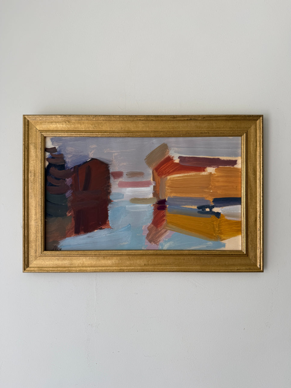A framed vintage abstract painting depicting stylized architectural forms in warm and cool tones, housed in a gold frame. Available at Hue.