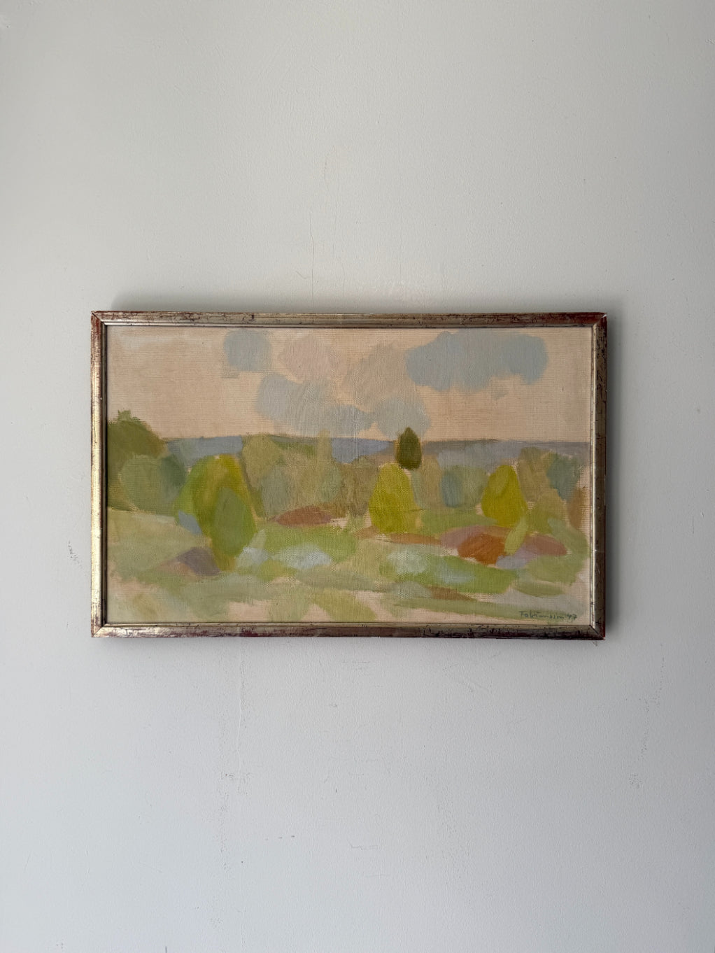 A framed vintage landscape oil painting. The painting depicts a green field with trees under a cloudy sky, enclosed in a rustic frame. Available at Hue. 