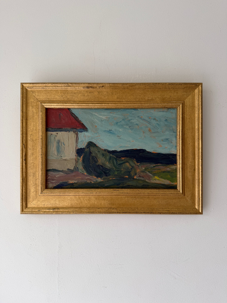 A framed vintage landscape oil painting featuring a white house with a red roof, dark hills, and a blue sky, housed in a gold fram. Available at Hue. 