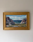 A framed vintage landscape oil painting depicting a rocky coastal path leading to the sea under a cloudy sky. Available at Hue.
